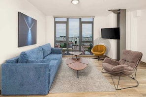 A modern living room with a sofa, a coffee table, a chair, and a TV mounted on the wall. - Jr. Apartment Upper Level (Panama City)