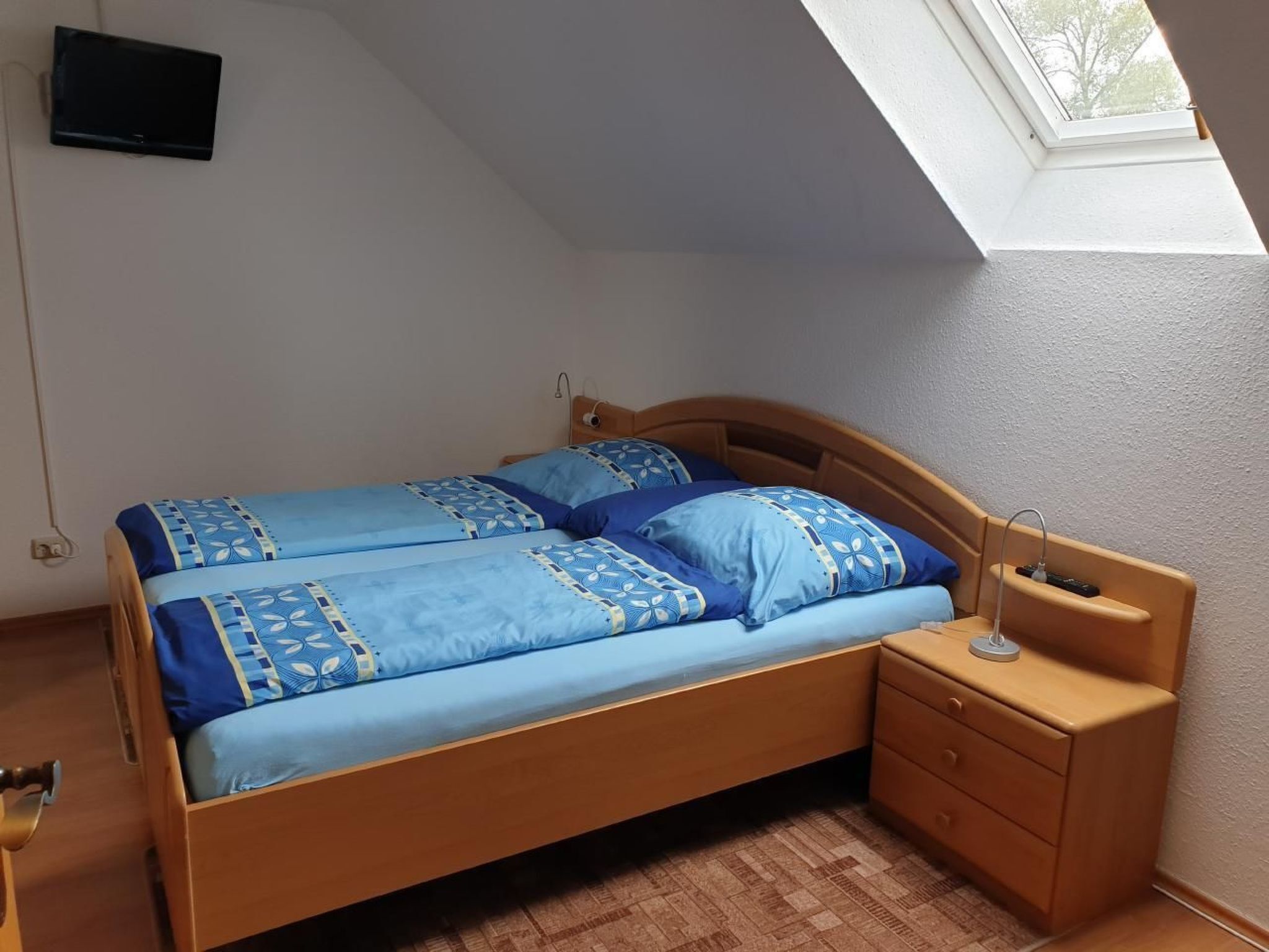 A bedroom with a wooden bed, blue bedding, a nightstand, and a skylight.