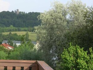 A view of a building with a red roof, surrounded by lush greenery and a hill with a castle-like structure in the background. - FeWo Landsbergblick by Interhome (Meiningen)