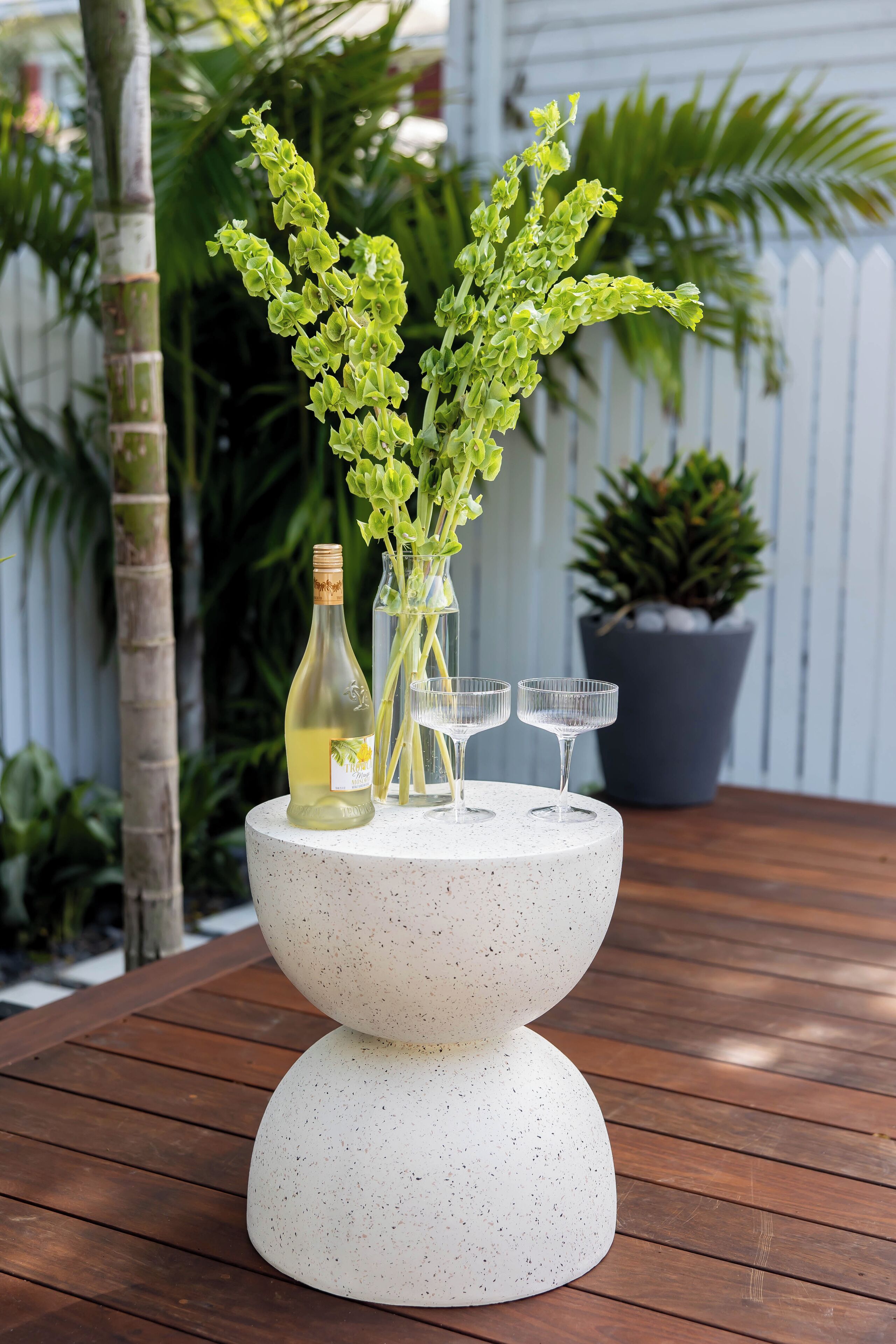 A table with a white speckled centerpiece, a bottle of white wine, and two clear wine glasses.