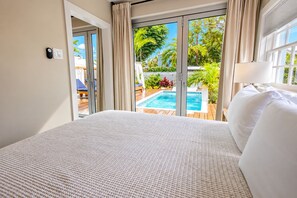 A hotel room with a large bed, a view of a swimming pool, and a sliding glass door. - Lighthouse Suites Collection (Key West)