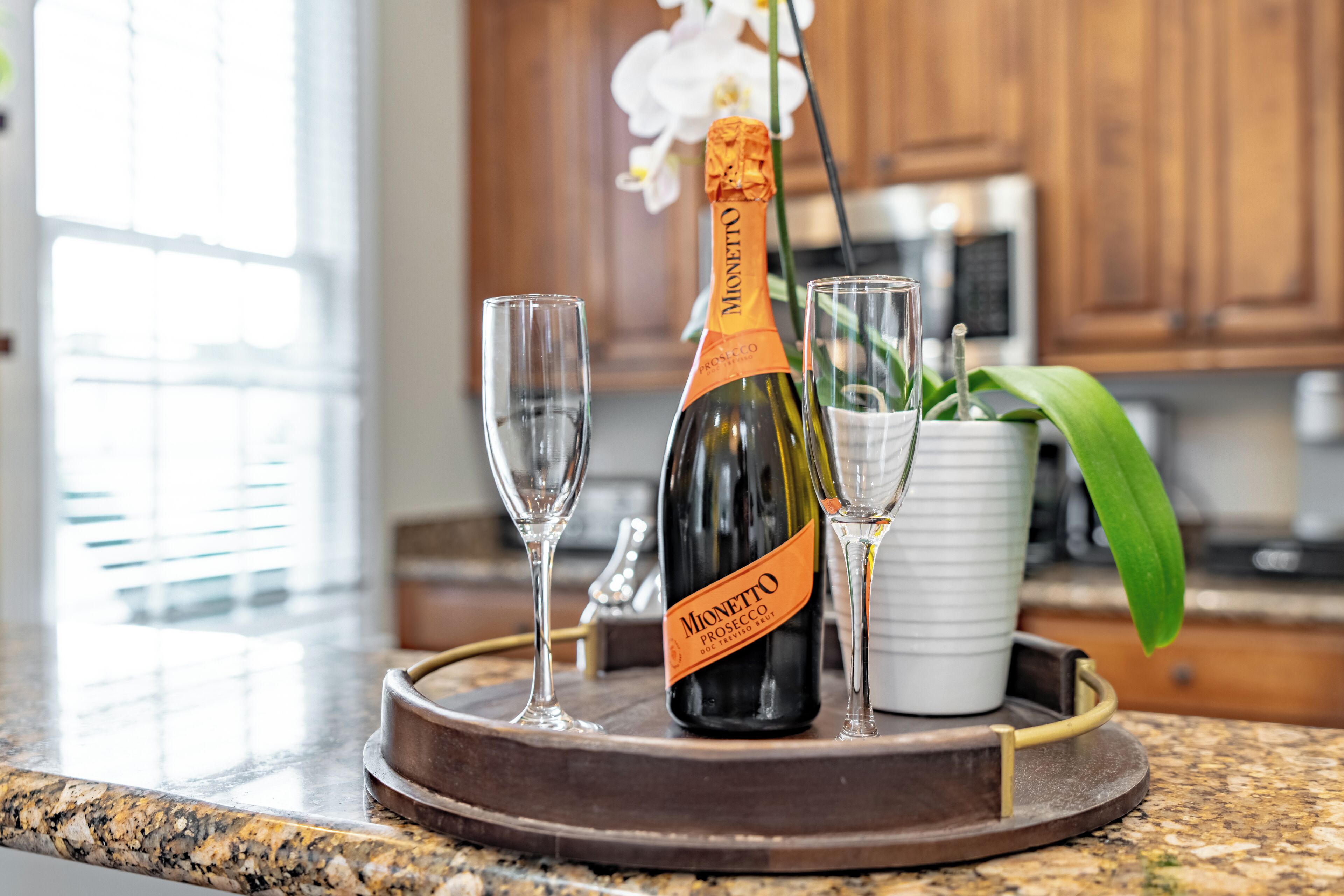 Una bottiglia di Prosecco Monetto su un vassoio con due bicchieri e un'orchidea in vaso.