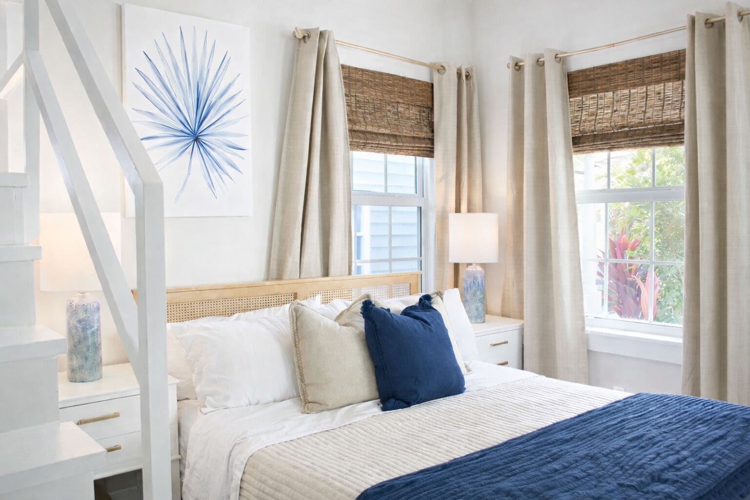 A bedroom with a bed, two bedside tables, a window with curtains, and a wall-mounted artwork.
