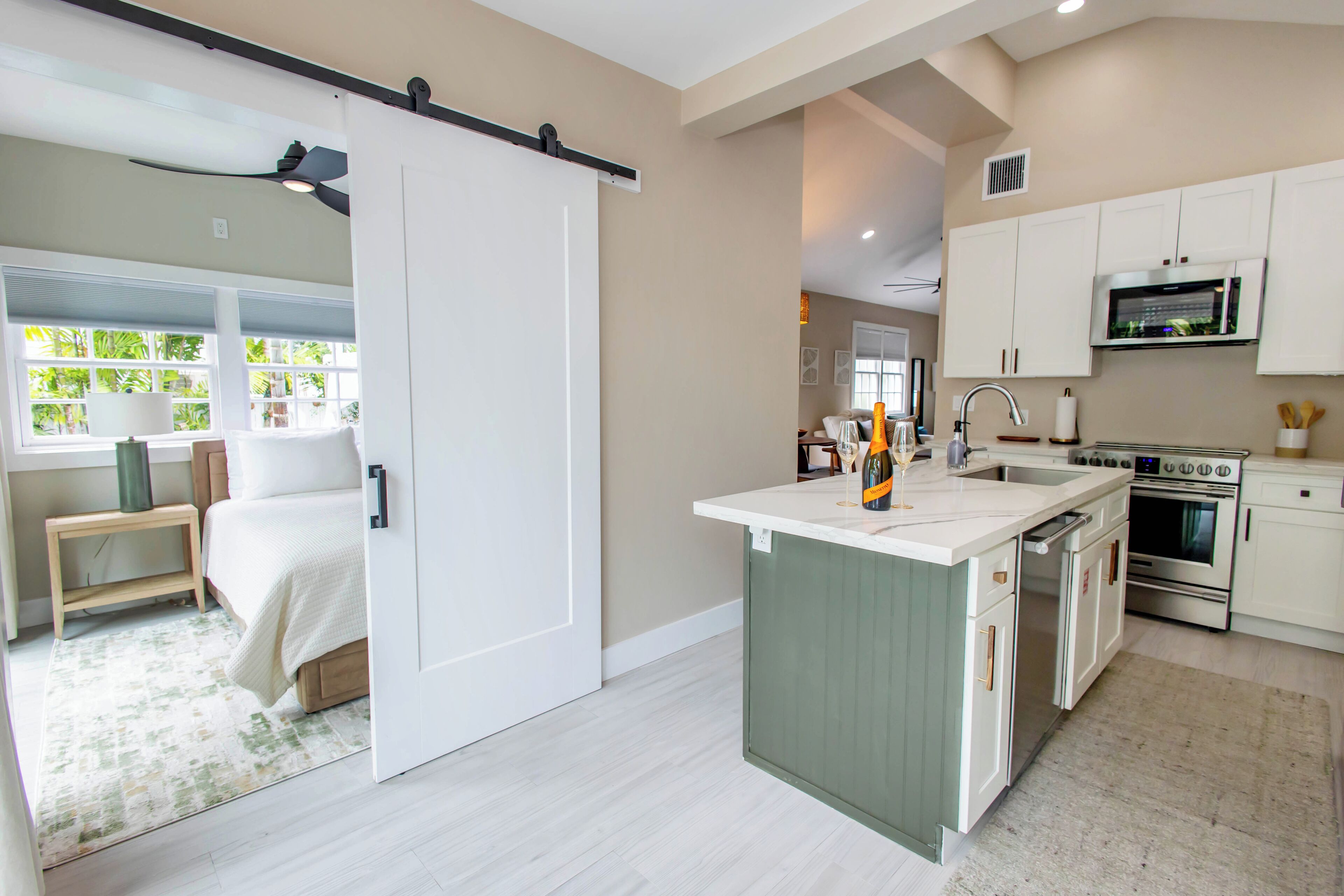 A modern kitchen with a central island, built-in appliances, and a sliding door leading to a bedroom.