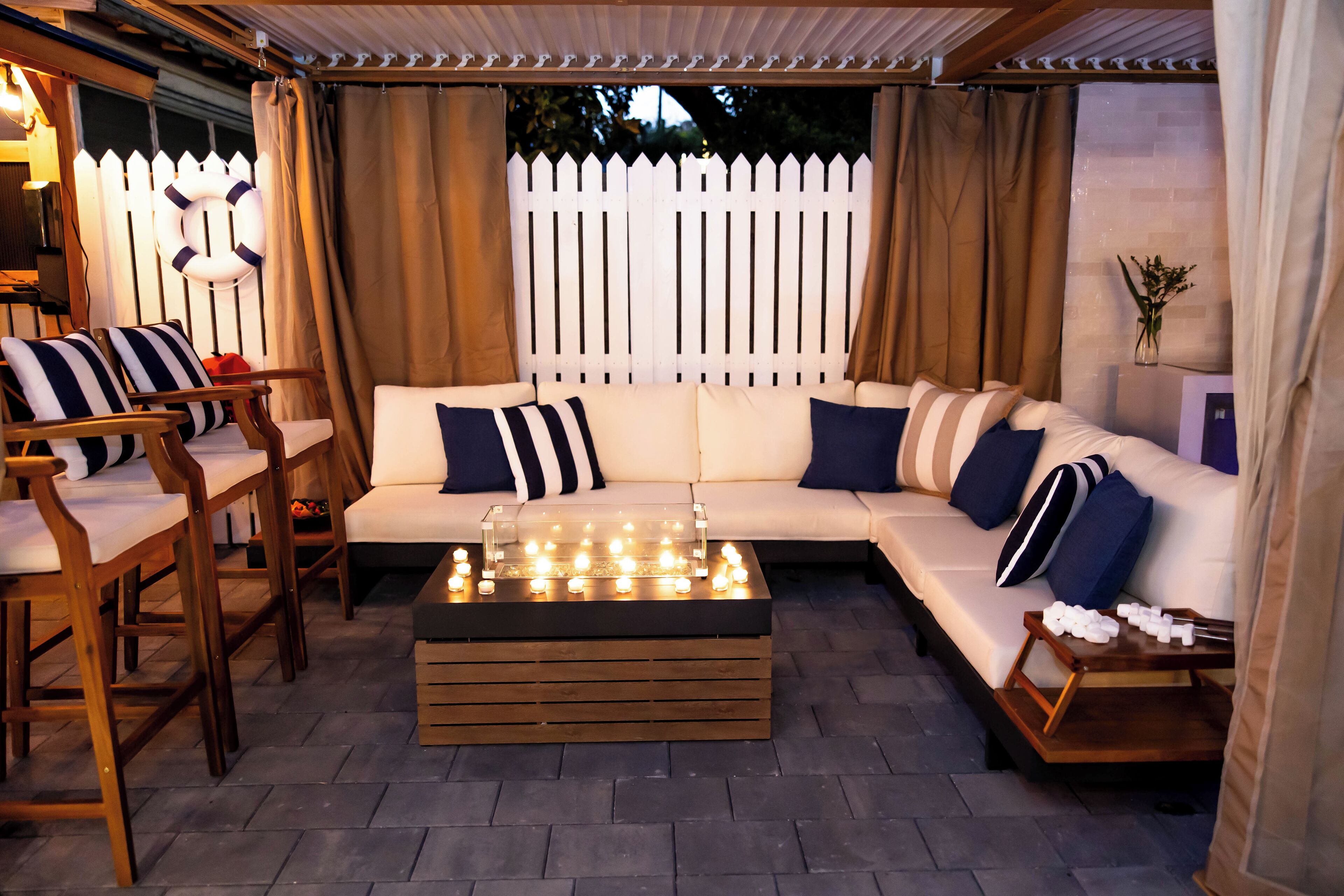 A cozy outdoor seating area with a white sofa, striped cushions, wooden chairs, and a coffee table with candles.