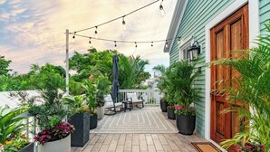 A covered outdoor patio with a wooden deck, potted plants, and string lights. - Lighthouse Suites Collection (Key West)