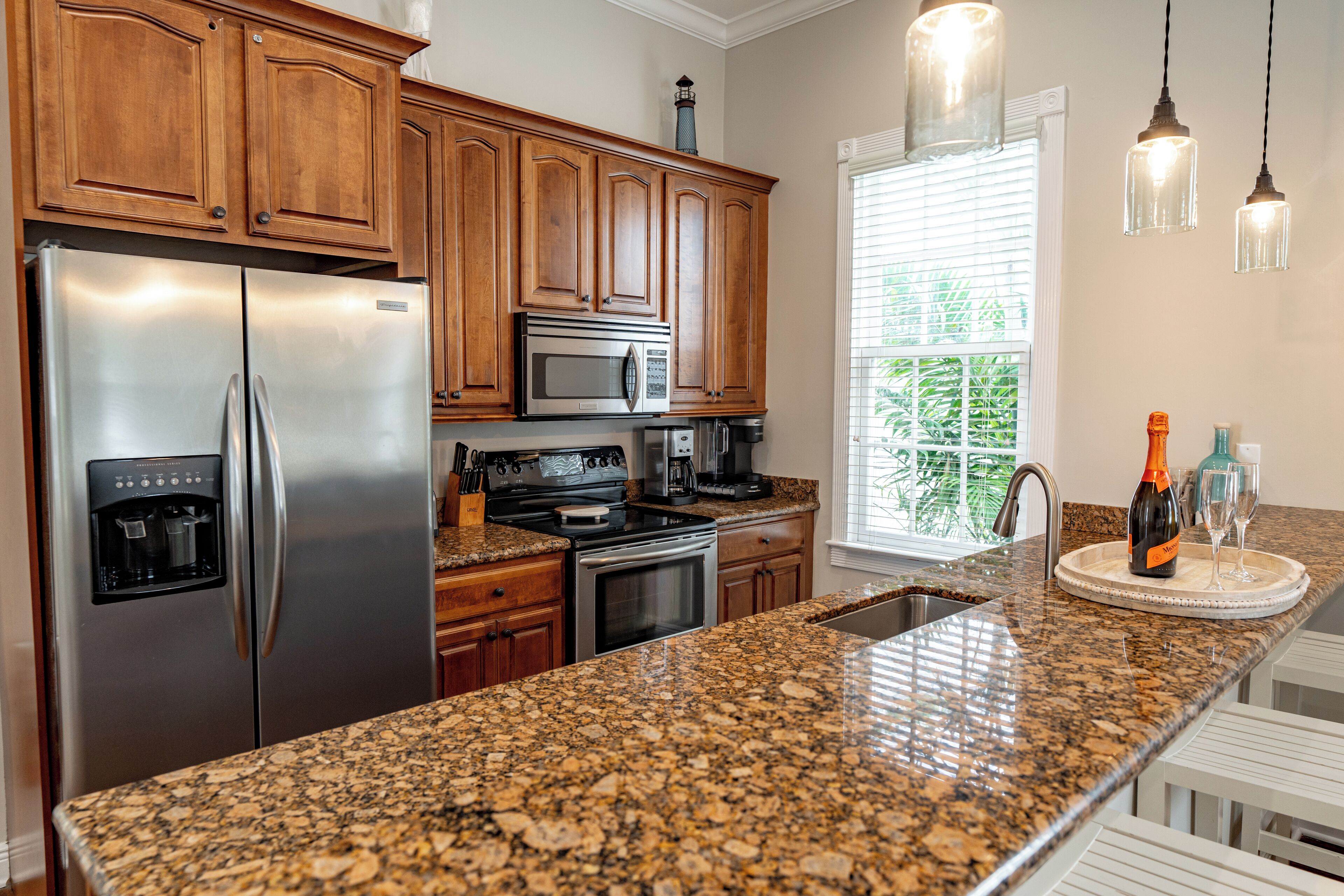A kitchen with granite countertops, stainless steel appliances, wooden cabinets, and pendant lighting.