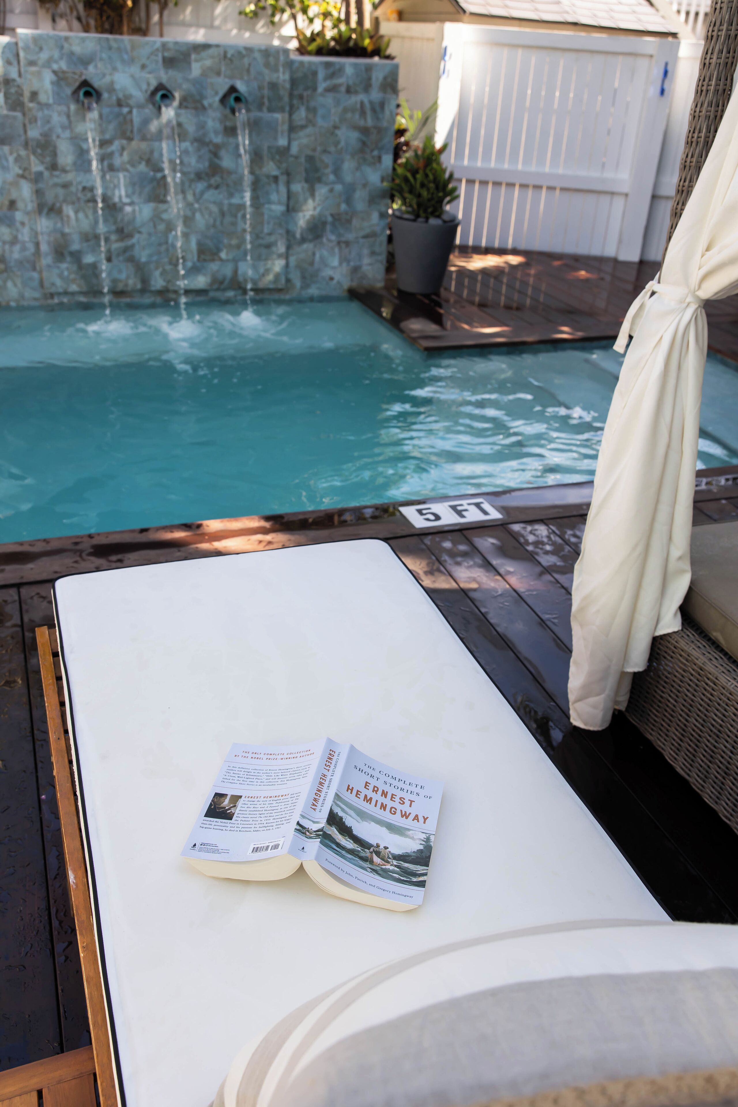 A poolside area with a lounge chair, a book, and a sign indicating the pool depth.
