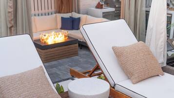 A deck with two white lounge chairs, a small round table, and a fire pit.