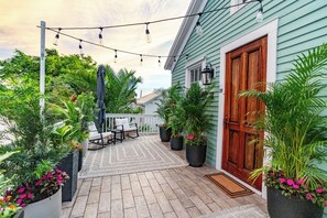 A covered patio with outdoor furniture, potted plants, and string lights.
