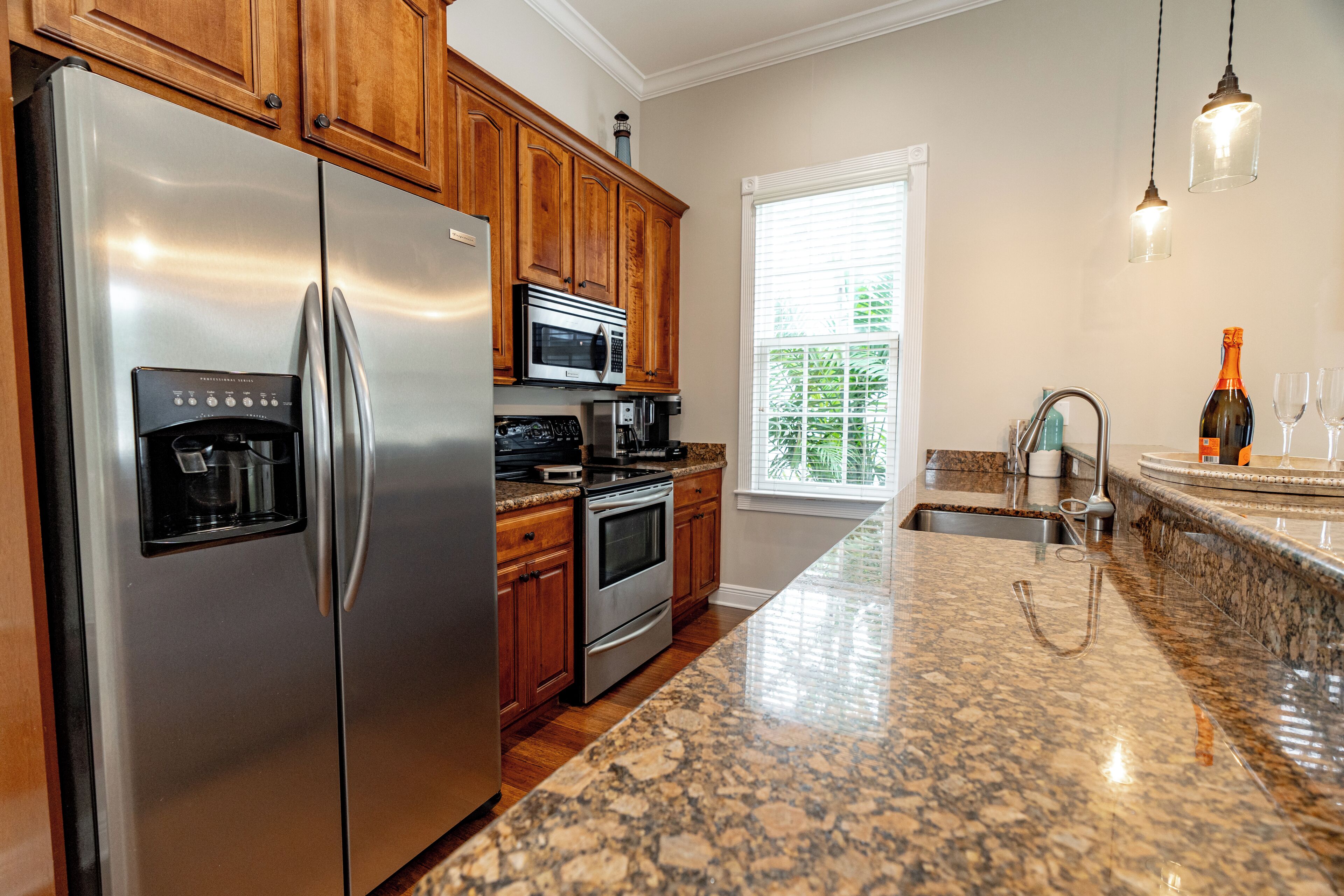A kitchen with stainless steel appliances, wooden cabinets, granite countertops, and a window with blinds.