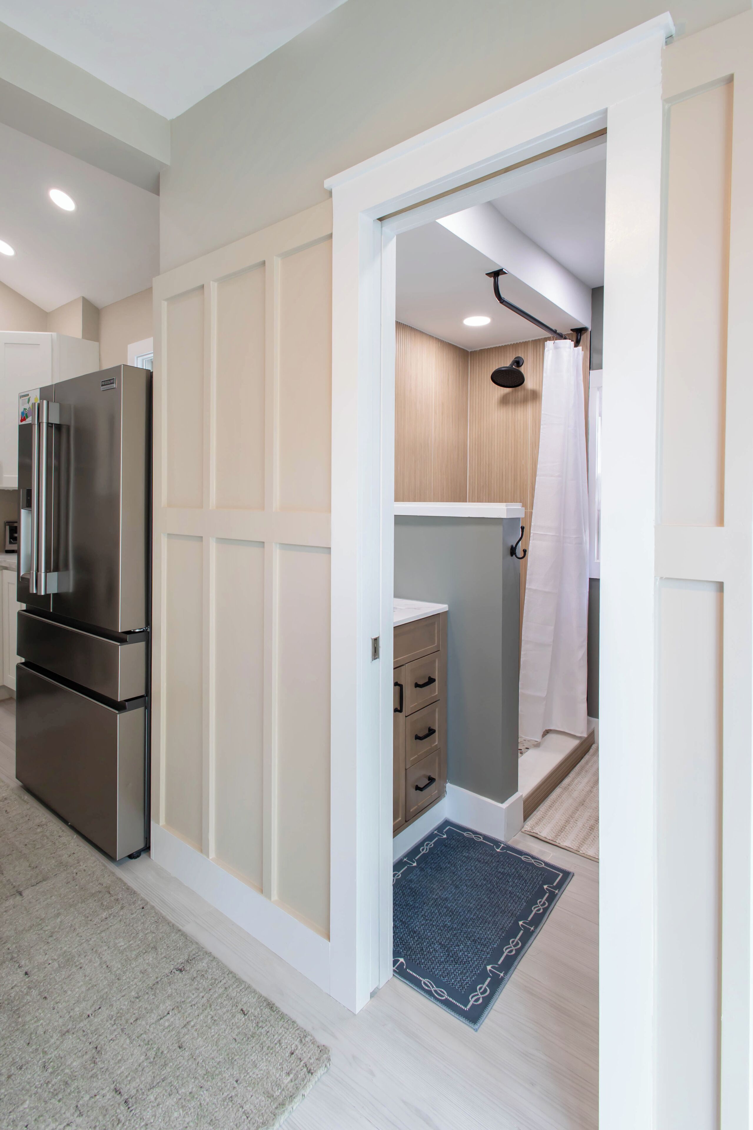 A modern kitchen with a stainless steel refrigerator, a wooden cabinet, and a bathroom with a shower curtain.