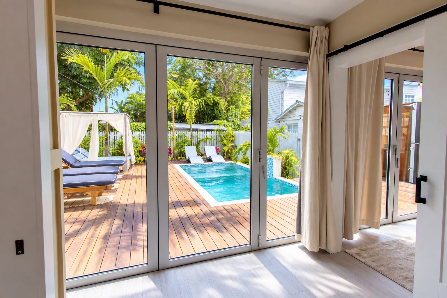 A modern room with a sliding glass door leading to an outdoor swimming pool area with lounge chairs and a canopy.