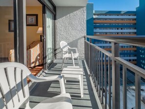 A balcony with white plastic chairs, a patterned sofa, and a view of a multi-story building. - Landmark 1006 (Myrtle Beach)
