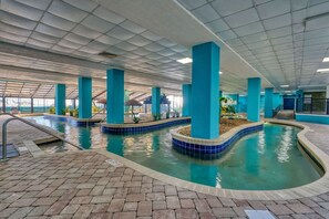 An indoor swimming pool with multiple lanes, surrounded by blue pillars, and a brick floor. - Landmark 1006 (Myrtle Beach)