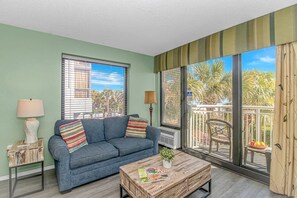 A living room with a sofa, two lamps, a coffee table, and large windows with blinds. - Sailfish 210 (Myrtle Beach)