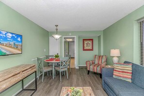 A living room with a dining table, chairs, a sofa, a TV, and a framed picture on the wall. - Sailfish 210 (Myrtle Beach)