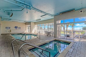 An indoor swimming pool with clear glass walls, a lifeguard sign, and a view of palm trees outside. - Sailfish 210 (Myrtle Beach)