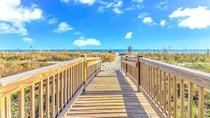 En træpromenade der fører til en strand med en klar himmel.