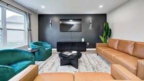 A modern living room with a large window, teal armchairs, a black coffee table, and a brown leather sofa. - Shuffleboard~Hot Tub~Arcade~Foosball~Spacious for Groups~7 Min to Ruoff (Noblesville)