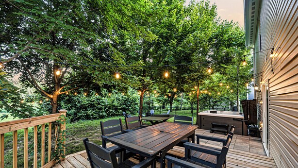 A wooden deck with a table and chairs, surrounded by trees and string lights. - Shuffleboard~Hot Tub~Arcade~Foosball~Spacious for Groups~7 Min to Ruoff (Noblesville)