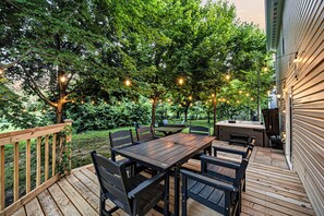 A wooden deck with a table and chairs, surrounded by trees and string lights.
