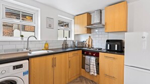 Cocina compacta con armarios de madera, horno integrado, lavaplatos y refrigerador.