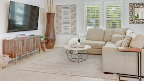 Een moderne woonkamer met een flatscreen televisie, een houten kast, een beige bank en een salontafel.