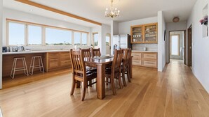 Uma cozinha ampla com piso de madeira, mesa de jantar com cadeiras e grandes janelas que proporcionam iluminação natural.