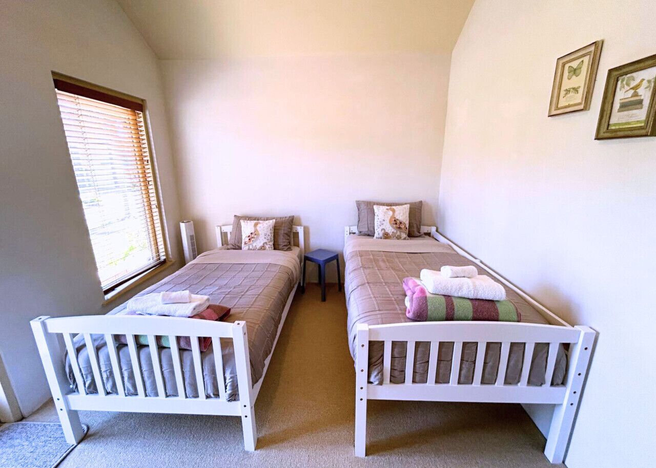 A room with two single beds, a small table, and a window with blinds.