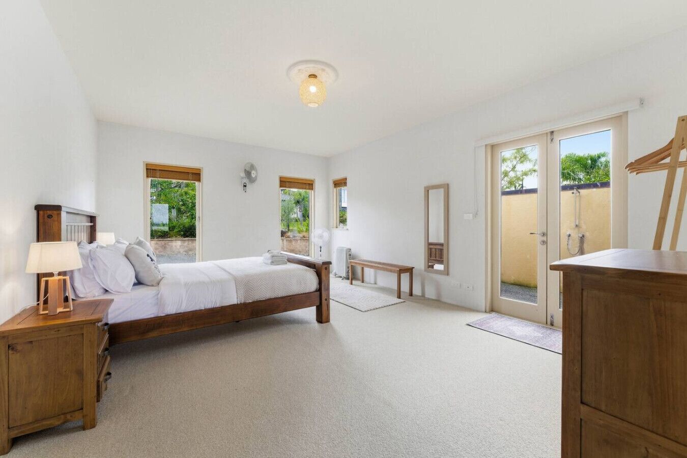 Une chambre à coucher avec un lit en bois, des tables de chevet, un banc et un grand miroir.
