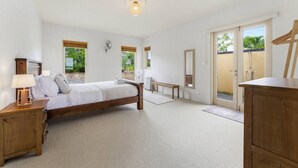 Um quarto com cama de madeira, mesas de cabeceira, um banco e um espelho grande.
