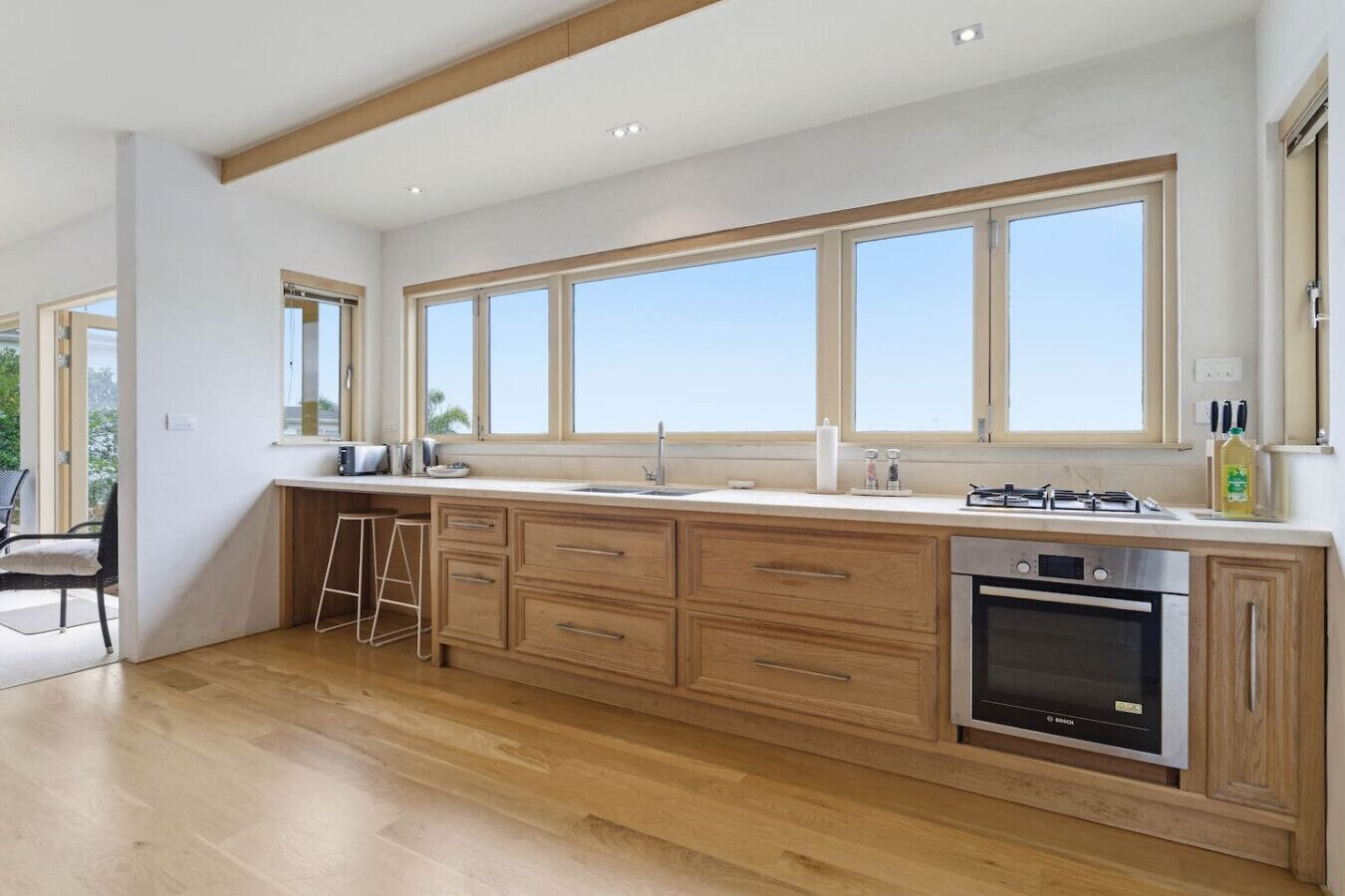 Une cuisine moderne avec des meubles en bois, un four encastré et une grande fenêtre donnant sur l’extérieur.