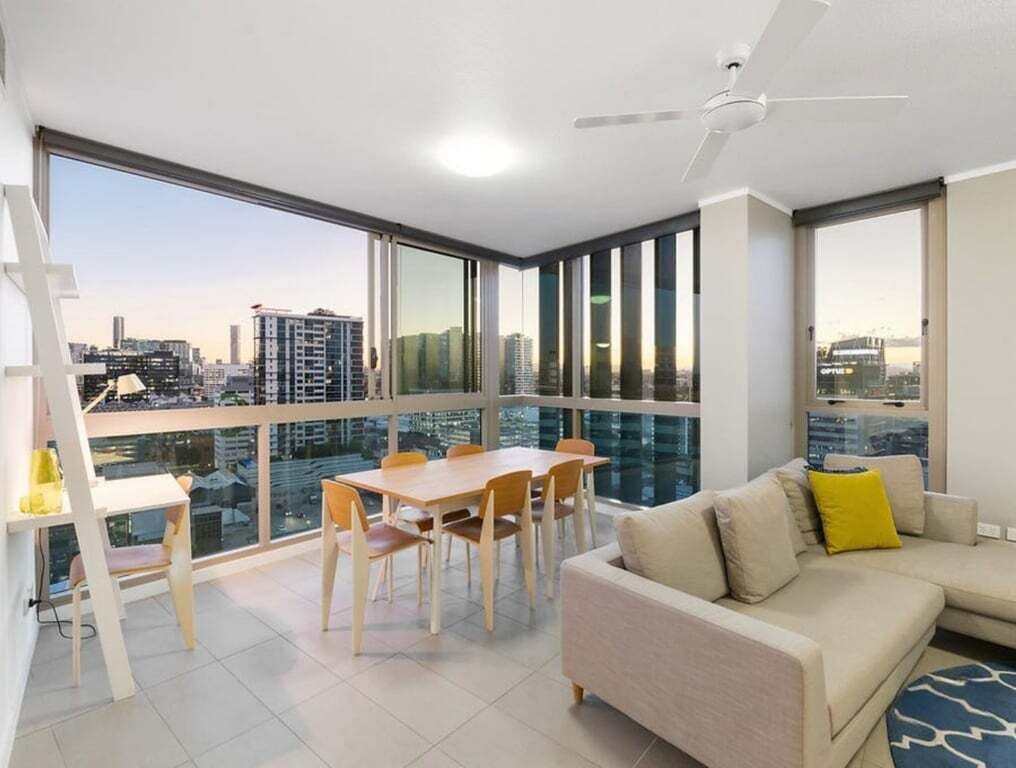 A modern living room with a balcony, a dining area, and a sofa with cushions.