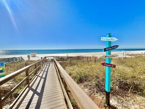 A wooden boardwalk leading to a beach with directional signs indicating 'Starkuck's', 'H2O Bar & Grill', 'Pools', and 'Towers 2'. - Modern Gulf View Condo w Bunks Sleeps 6 at Majestic Beach Resort! (Panama City Beach)
