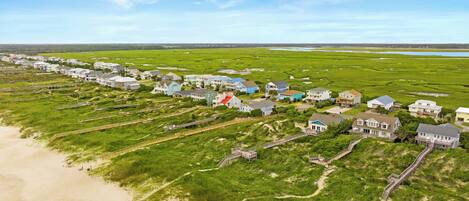 Vista aérea de una zona residencial costera con casas conectadas por pasarelas de madera, una playa y un paisaje pantanoso.