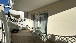 Varanda com mesa e cadeiras, um vaso de planta e vista para a rua.