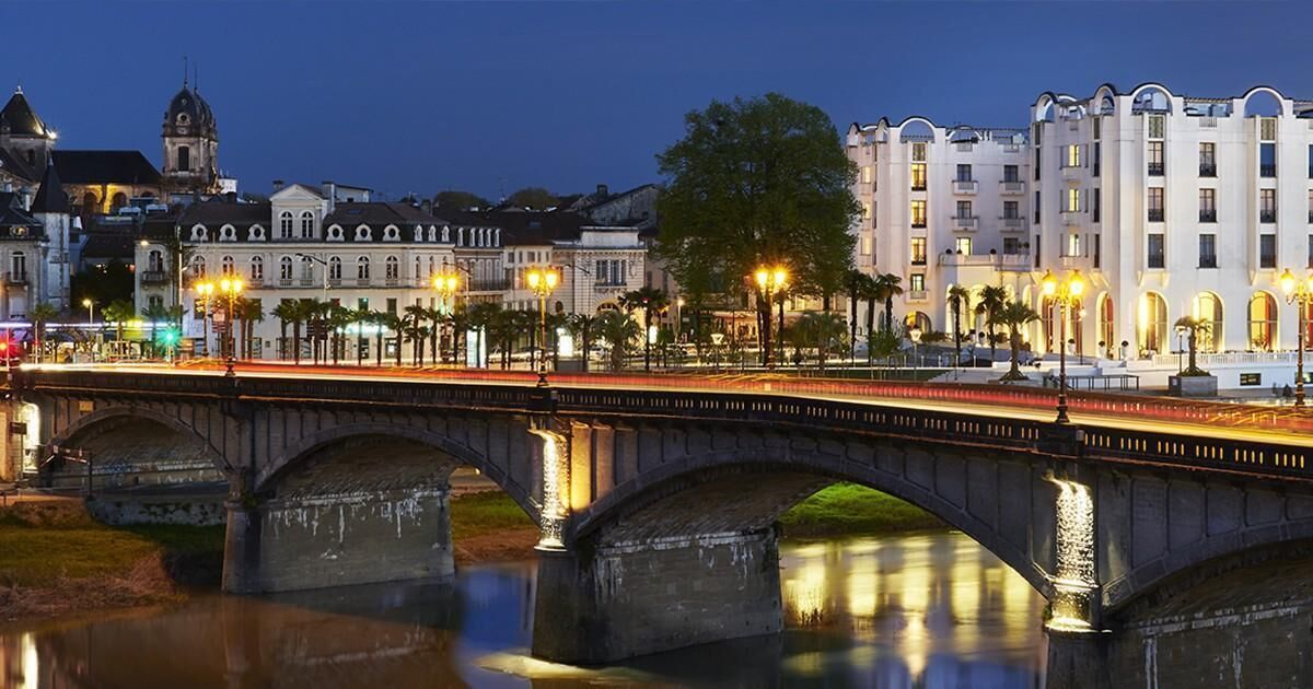 Un puente de piedra sobre un río tranquilo de noche, con edificios históricos y faroles a ambos lados.
