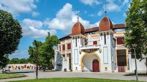 Um edifício histórico com fachada simétrica, um arco central e duas torres em cúpula.