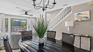 A dining area with a chandelier, a potted plant, wicker chairs, and a view of the outdoors. - PRIVATE BEACH - Two Bikes - Newly renovated - 7 Palms 3 (Panama City Beach)