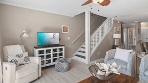 A living room with a sofa, ottoman, TV, cabinet, and a ceiling fan. - PRIVATE BEACH - Two Bikes - Newly renovated - 7 Palms 3 (Panama City Beach)