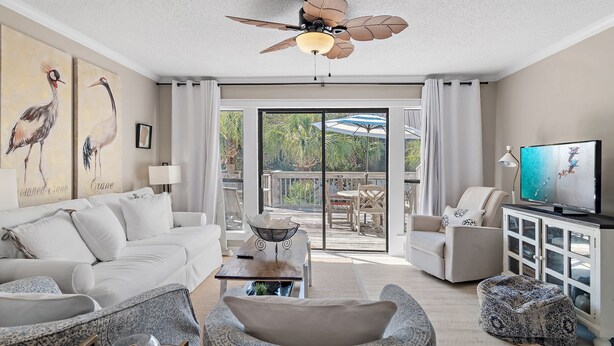 A living room with a ceiling fan, a sofa, a coffee table, a TV, and a balcony with outdoor furniture. - PRIVATE BEACH - Two Bikes - Newly renovated - 7 Palms 3 (Panama City Beach)