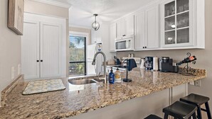 A kitchen with white cabinets, a granite countertop, a sink, a microwave, and a coffee maker. - PRIVATE BEACH - Two Bikes - Newly renovated - 7 Palms 3 (Panama City Beach)