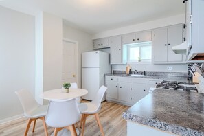 A modern kitchen with white cabinets, a granite countertop, and a dining area with white chairs.