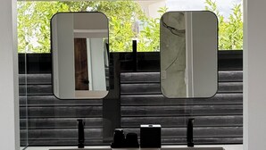 A modern bathroom with a double sink, two mirrors, and a view of greenery outside. - Luxury Bungalow + Private Infinity Pool + Firepit (Long Bay Hills)