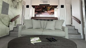 A modern living room with a large flat-screen TV, a round wooden coffee table, and a grey sofa. - Luxury Bungalow + Private Infinity Pool + Firepit (Long Bay Hills)
