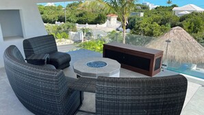 A balcony with wicker furniture, a fire pit, and a view of the ocean and greenery. - Luxury Bungalow + Private Infinity Pool + Firepit (Long Bay Hills)