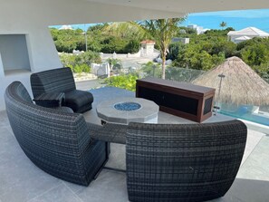 Ein Balkon mit Rattanmöbeln, einer Feuerstelle und Blick auf Meer und Grünflächen.