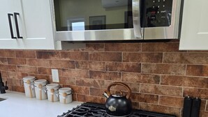 A kitchen with a stainless steel stove, oven, and microwave. There are jars on the counter and a kettle on the stove. - The Hidden Gem (Saint Albans)