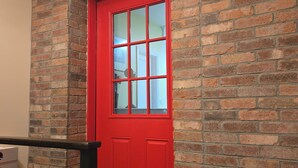 A red door with a glass panel, set in a brick wall with a decorative element above it. - The Hidden Gem (Saint Albans)